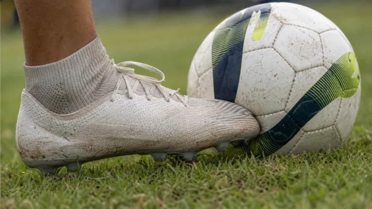 Close no cabedal em tecido knit de uma chuteira tocando a bola em gramado natural